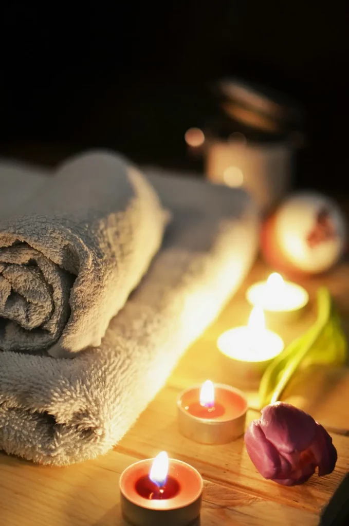 Des serviettes douces et enroulées à côté de bougies lumineuses et d'une tulipe violette créent une atmosphère paisible et relaxante sur une surface en bois.