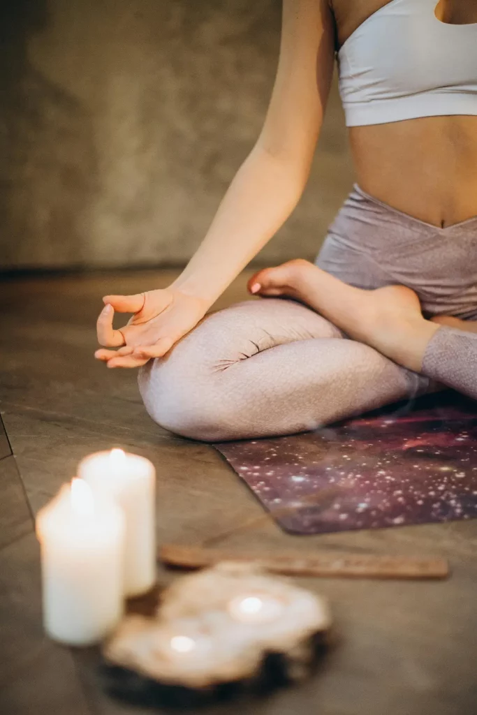 Une femme pratique le yoga dans un cadre serein, assise les jambes croisées, avec des bougies et de l'encens à proximité, incarnant la tranquillité et la concentration.